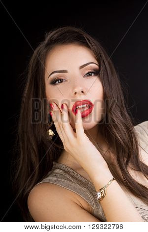 Young brunette woman in evening dress with beautiful make-up  touches her lips in desire on black background. Looking at camera