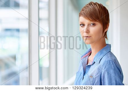 Portrait of a modern young woman looking at the camera with a keen and serious expression, in a corridor with bright natural light