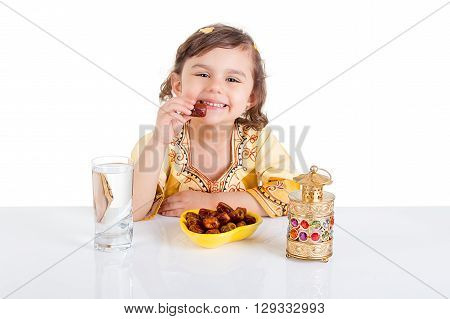 Young Muslim girl eating dates for brakfast in Ramadan - sitting on a table with water , dates , Quran, and Ramadan lantern