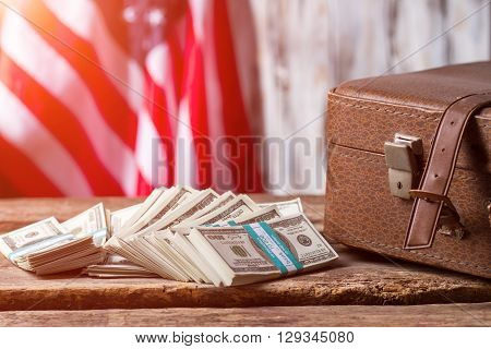 US flag, case and dollars. Cash bundles near brown case. There's never enough money. Taxes payed by citizens.