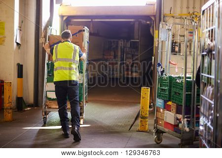 Man pushing roll cage into a truck at a warehouse, back view