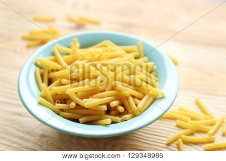 Dry maccheroni pasta in blue plate on wooden table