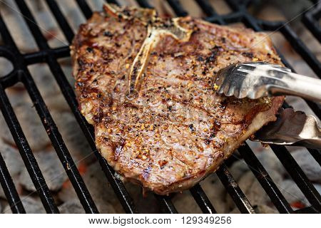 Tbone beef steak being cooked on a grill with tongs