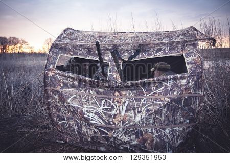 Hunting tent with hunters waiting for prey in reed bushes next to the river during sunrises. Gun barrels  stick out from tent window