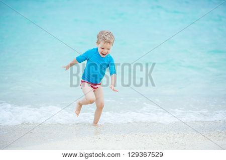 Happy little boy running in breaking waves on the beach