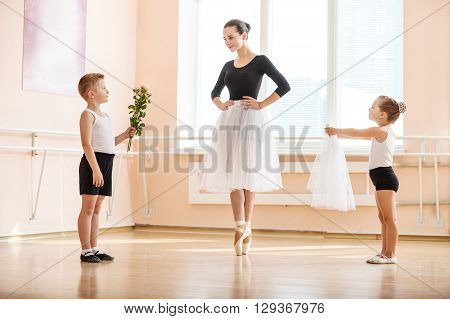 At ballet dancing class: young boy and girl giving flowers and veil to older student while she is dancing en pointe