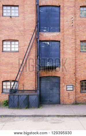 Old style red brick building and three metal doors and windows on it and old hoist