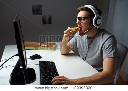 technology, gaming, entertainment, let's play and people concept - young man in headset with pc computer eating pizza while playing game at home and streaming playthrough or walkthrough video