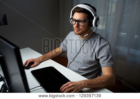technology, gaming, entertainment, let's play and people concept - young man in headset and glasses with pc computer playing game at home and streaming playthrough or walkthrough video