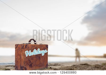 Woman in sweater walking on beach against suitcase with the message holidays