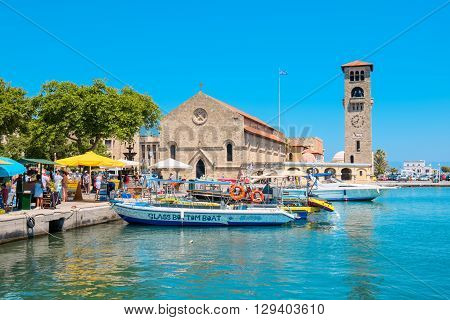 RHODES GREECE - JULY 4 2015: Tourists walking in Mandraki harbour near Church of the Evangelismos (Annunciation)