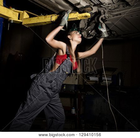 Beautiful young female mechanic inspecting car in auto repair shop. Sexy mechanic.