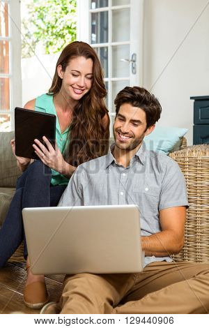 Happy young couple using digital tablet and laptop in living room