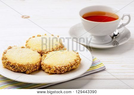 Butter cookies (alfajores) with caramel and peanut and cup of tea on wooden background.