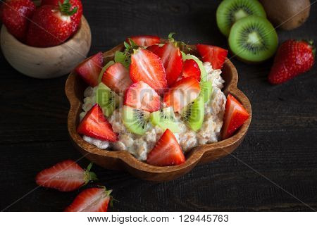 Oatmeal porrige with strawberries and kiwi fruit in a wooden bowl. Rustic Style