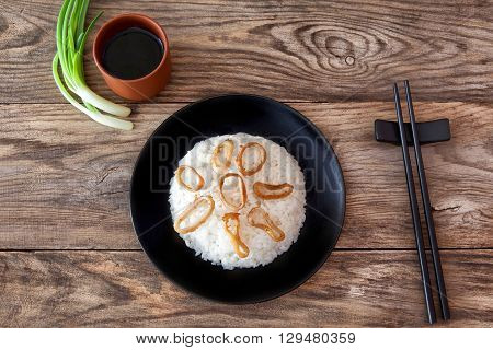 Spicy stir fried squid with rice and green onion and chopstick on black bowl on rustic brown wooden background