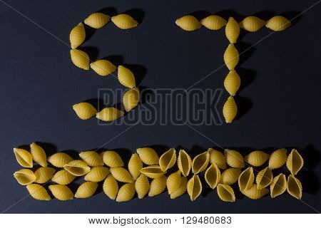 English alphabet laid out in the form of pasta shells on a dark background .