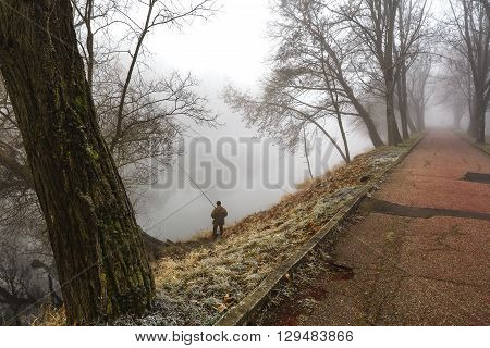 A lone man fishing in the morning hours when autumn fog on the river.