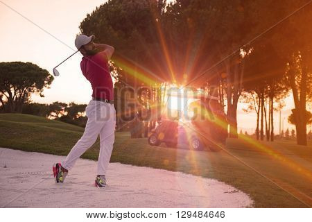 golf player shot ball from sand bunker at course with beautiful sunset with sun flare