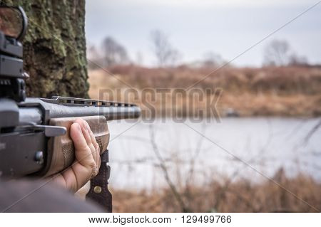 Hand holding shotgun aiming and ready to shot during hunting with copy space