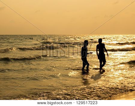 silhouette of two people walking on beach at sunset