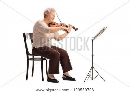 Mature female violinist playing a violin seated on a wooden chair isolated on white background