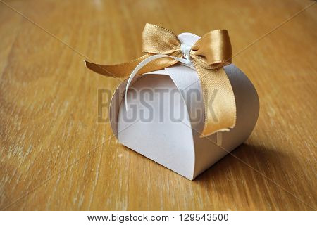 Small gift box made of paper with a colorful ribbon topnot atop on a wooden background