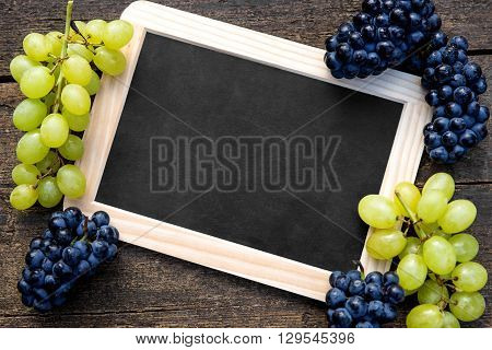 White and blue grapes and a slate with copyspace on wooden table