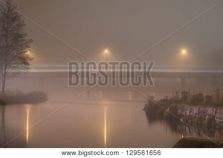Bridge over water in thick november fog. Long exposure time shows lines from traffic.