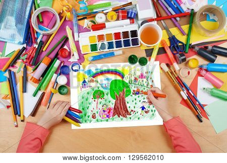 people relax on meadow near the village, child drawing, top view hands with pencil painting picture on paper, artwork workplace
