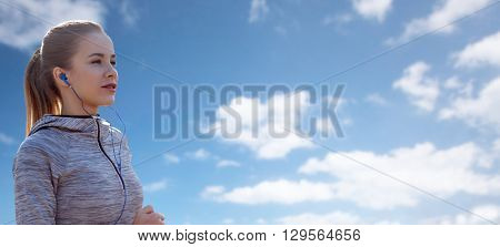 fitness, sport, people, technology and lifestyle concept - happy woman running and listening to music in earphones over blue sky and clouds background