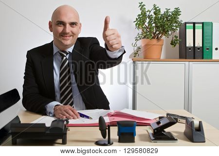 Successful manager holds up thumb. He is smiling.