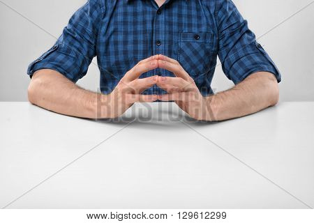 Cropped portrait of a man sitting with his clasped fingers. Readiness to talk. Symbols and gestures. Body language. Hand gesture. Readiness for work. Listen attentively. Straight posture.