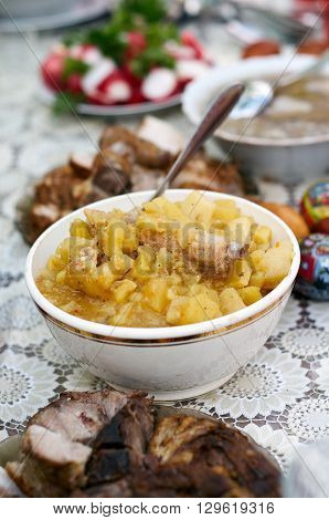 Vertical selective focus shot of an assortment of meals. Mashed Potato with pork ribs in bowl with serving spoons. Meal accompanied with slices of boiled salted pork sausage boiled eggs radish fresh vegetables