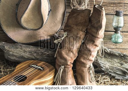Closeup american west rodeo brown felt cowboy hat and traditional leather boots with ukulele in vintage ranch barn background Still life style