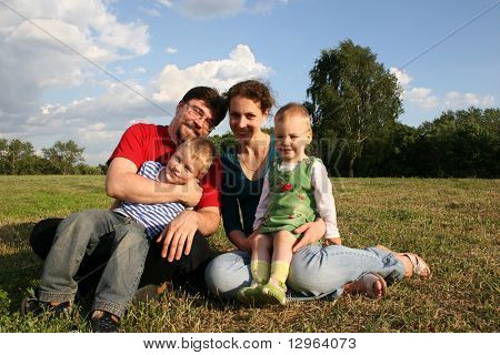 famiglia con due bambini seduti sul prato e alberi 2
