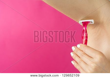 Woman shaving her armpit with a red shaver