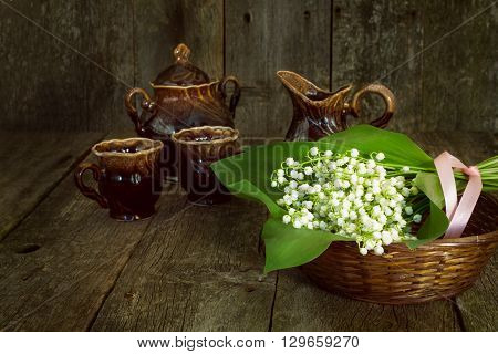 bouquet of lilies of the valley in a basket with cups and sugar bowl on the old wooden background blurred. toned photo