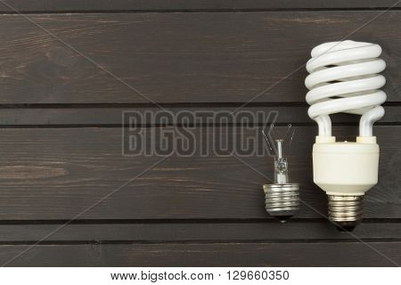 Broken incandescent bulbs and new energy-saving light bulb on wooden background. Sales of light bulbs. Advertising on lighting technology.