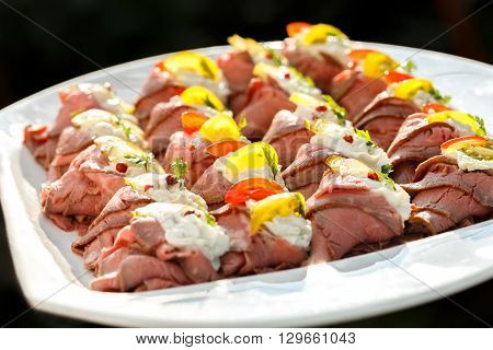 Plate Of Sliced, Rolled And Garnished Roast Beef Canapes. On Black Background.