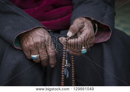 Old Tibetan woman holding buddhist rosary in Hemis monastery Ladakh India. Hand and rosary close up
