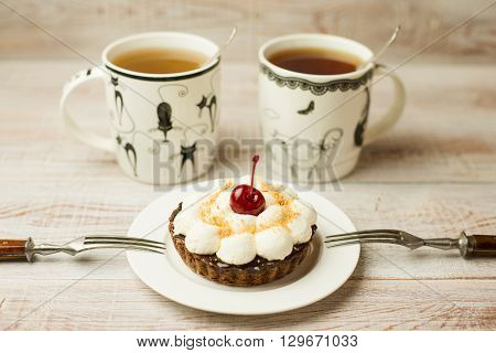 Two Cup of tea and cake with a cherry on the table