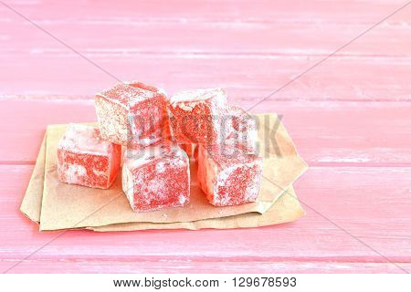 Sweet pieces of turkish delight on the wrapping paper and pink wood background