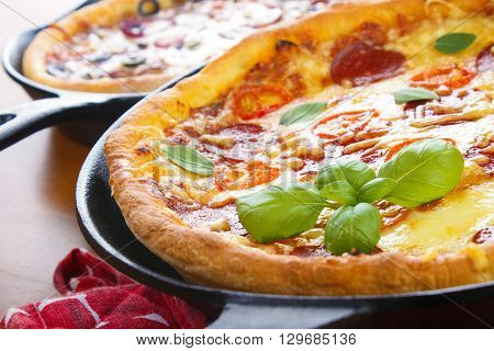 Cast iron skillet pan pizzas on wooden tabble closeup