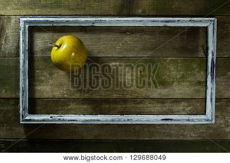Apple in the old frame on a wooden background