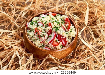 Homemade Fresh Couscous salad with vegetables wooden bowl on straw