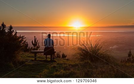 Man on a seat watching the sun go down over the town of Levin New Zealand