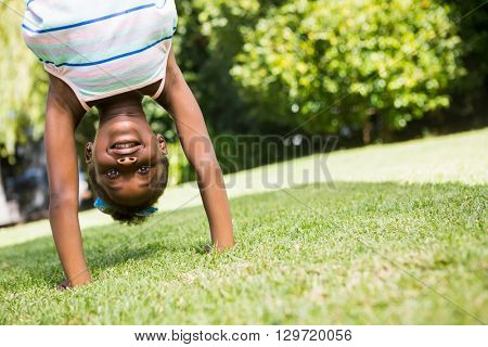 Portrait of a cute mixed-race girl smiling and doing a headstand on a park