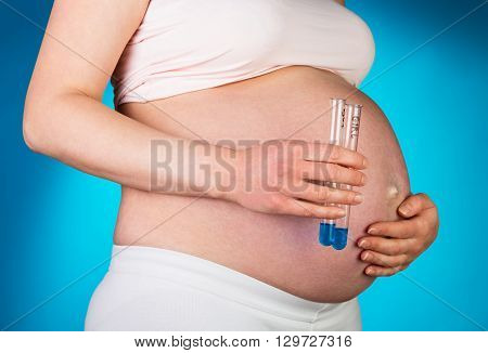 Pregnant woman with IVF on a blue background with test tubes in hand