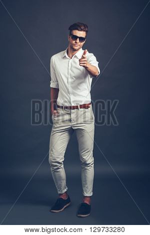 Maybe you? Full length of confident young handsome man  pointing you and looking at camera while standing against grey background
